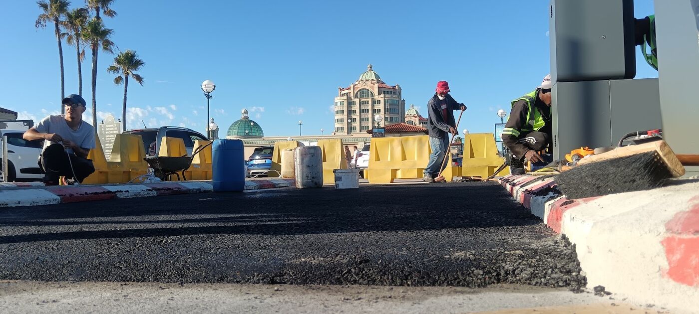 Team compacting fresh asphalt with barriers in place